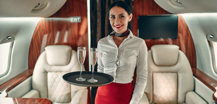 a crew member on a private jet holding a tray of champagne