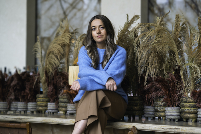 Franky Rousell, CEO of JOLIE design, sitting in a cafe space wearing a bright blue jumper