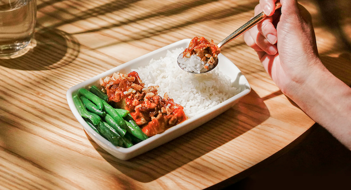 A white inflight dish containing Panang dry curry tofu with cashews and coconut rice