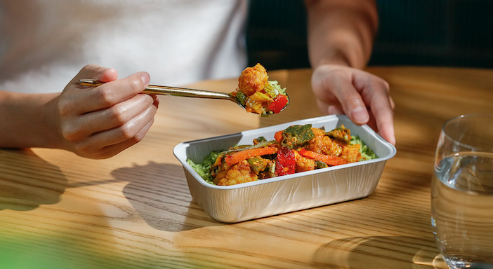 A foil dish containing vegetable masala with green pulao rice