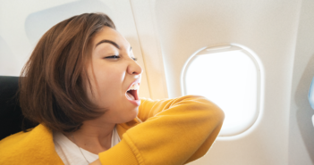 a woman on an aeroplane, sneezing into her sleeve