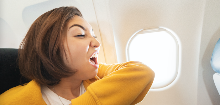 a woman on an aeroplane, sneezing into her sleeve