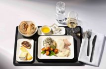 A black airline meal tray with white plates featuring luxury foods
