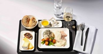 A black airline meal tray with white plates featuring luxury foods