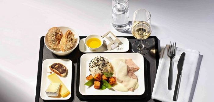 A black airline meal tray with white plates featuring luxury foods